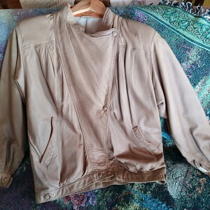 Puede incluir: Una chaqueta de cuero marr&oacute;n claro con cierre de cremallera y un bot&oacute;n a presi&oacute;n en el cuello. La chaqueta tiene dos bolsillos en la parte delantera y una manga larga.