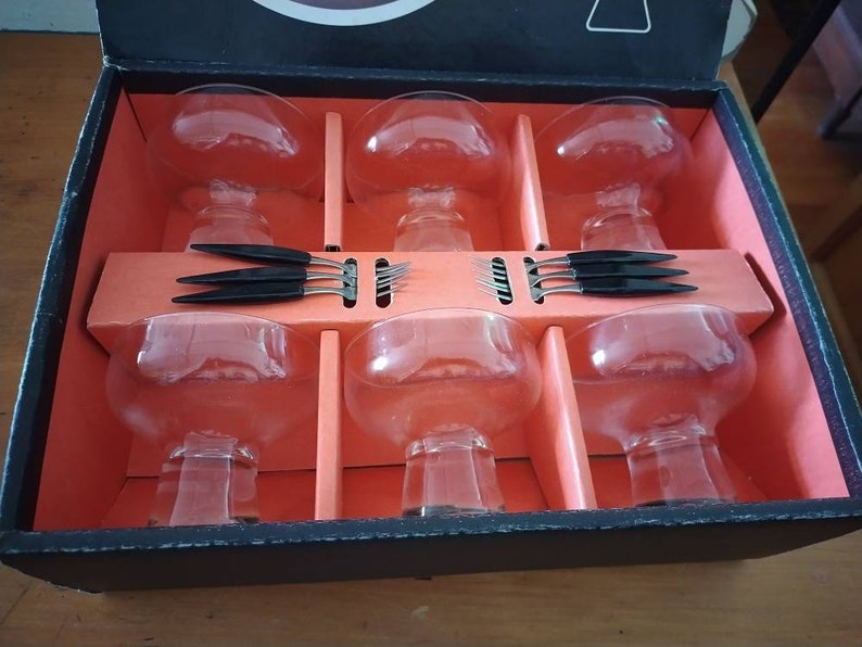 Puede incluir: Un juego de seis vasos de vidrio transparente con asas negras, empaquetados en una caja negra con interior rojo. Los vasos est&aacute;n dispuestos en dos filas de tres, con las asas hacia afuera. La caja est&aacute; abierta, revelando los vasos.