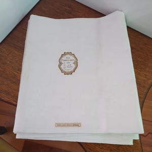 以下が含まれることがあります： 「All Pure Linen」と「Irish Linen Double Damask」と書かれた金色のラベルが付いた白いリネン製のテーブルクロスです。