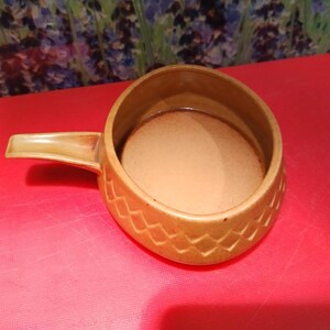 May include: A brown ceramic bowl with a handle. The bowl has a textured pattern on the outside.