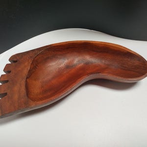 May include: A wooden bowl shaped like a foot with a carved design. The bowl is made of dark brown wood and has a smooth, polished finish.