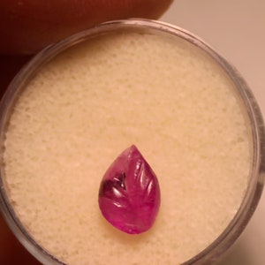 May include: A carved pink gemstone in the shape of a leaf, displayed on a white background.