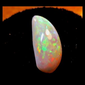 May include: A teardrop-shaped opal gemstone with a white body color and iridescent flashes of green, orange, and red.