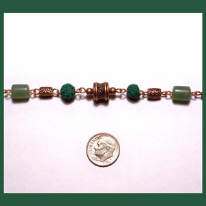 May include: A green and copper beaded necklace with a decorative copper charm. The necklace is about the size of a dime.