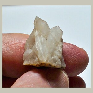 May include: A cluster of clear quartz crystals with a rough, natural texture. The crystals are clustered together in a small, irregular shape.