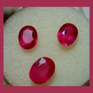 May include: Three oval-shaped, deep red gemstones on a white background.