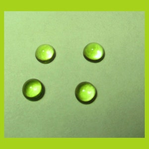 May include: Four green glass cabochons on a light green background.