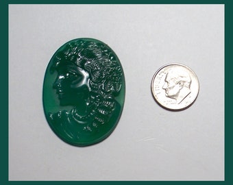 May include: A green cameo carved with a detailed profile of a woman's face. The cameo is oval shaped and about the size of a US dime.