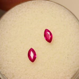 May include: Two pink marquise-shaped gemstones on a white background.