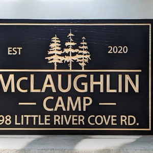 May include: Black wooden sign with gold lettering that reads "EST 2020 McLaughlin Camp 598 Little River Cove Rd.". The sign features a stylised image of three pine trees.