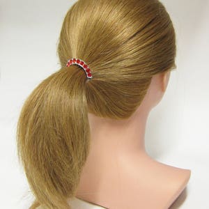 May include: A red rhinestone ponytail holder with a silver metal base.