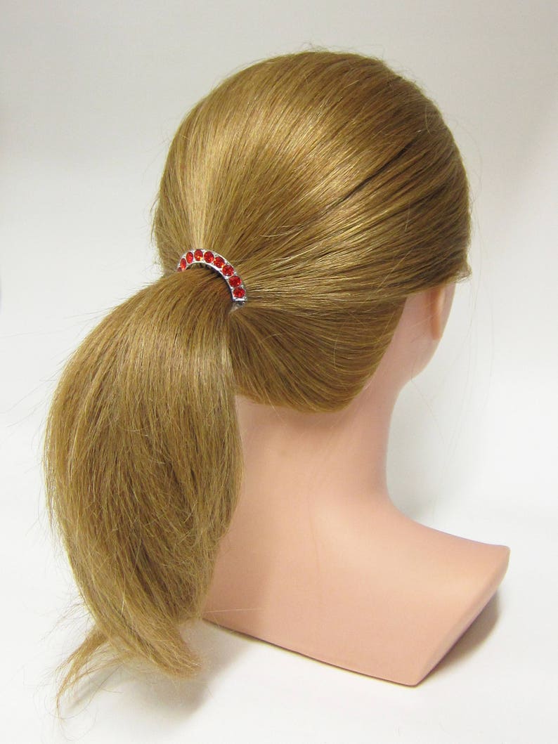 May include: A red rhinestone ponytail holder with a silver metal base.