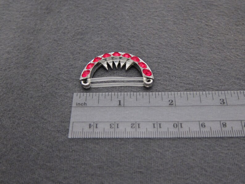 May include: A silver hair clip with a row of red rhinestones in the shape of an arch. The clip is about 1 inch wide and has a clear elastic band.