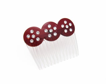 Può includere: Un pettine per capelli rosso con tre pezzi rotondi decorativi. Ogni pezzo è adornato con strass trasparenti.