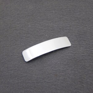 May include: A silver-colored metal hair clip, shaped like a rectangle with rounded edges.