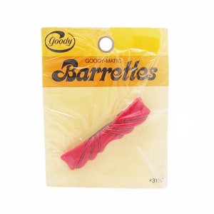 May include: A red plastic barrette with a wavy design. The barrette is packaged on a yellow card with the text "Goody-Matic Barrettes #315".
