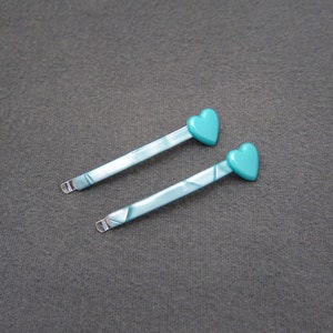 May include: Two turquoise heart-shaped hair clips with a marbled pattern.