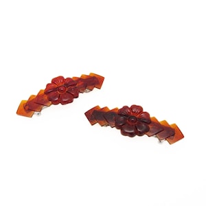 May include: A pair of brown hair clips with a carved flower design. The clips are made of plastic and have a shiny finish.