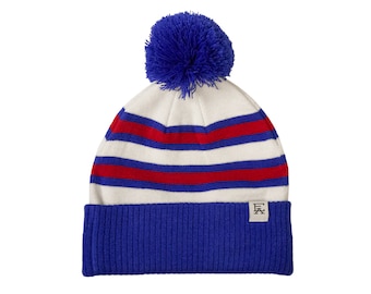 May include: White and blue striped knit beanie with a red stripe and a blue pom pom on top. The beanie has a blue fold-over cuff with a small white label that says "EA".
