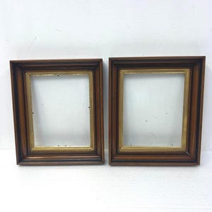 May include: Two rectangular picture frames featuring a dark brown wood finish with a stepped profile. Each frame includes an inner border of metallic gold trim. The frames are empty, showing a hollow center, and are positioned side by side.