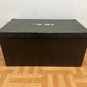 May include: A rectangular, dark green wooden storage chest with the text "198 MED" in white on the lid. The chest has metal corner reinforcements and sits on a parquet floor. The overall aesthetic is vintage.