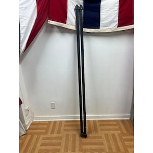 May include: Two long, slender, black wooden poles positioned vertically. Each pole features a flat, rectangular profile with a small, square-shaped decorative finial at the top end. The poles are straight and uniform in color, standing parallel to each other.