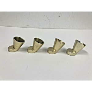 May include: Four small, gold-colored metal objects. Each has a rounded base and a cone-shaped top that angles upward. The objects are evenly spaced and appear to be decorative or functional items.