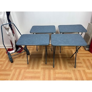May include: A set of four rectangular blue TV tray tables with rounded corners and thin metal legs, accompanied by a matching blue metal storage rack with wheels for organizing and transporting the folding tables when not in use.