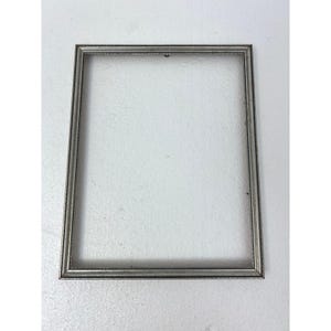 May include: A rectangular silver picture frame with a detailed border. The frame is empty, with a simple design and a neutral color, suitable for various types of artwork or photographs. The frame is made of metal.