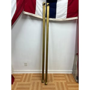 May include: Two long, slender, vertical metal rods with a metallic gold finish. Each rod features a small, angled bracket at the top and a flat, circular base at the bottom. The rods are positioned parallel to each other, standing upright.