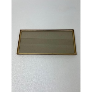 May include: A rectangular picture frame with a thin, metallic gold-toned border and a clear glass center. The frame has a simple, clean-lined design with sharp corners and a flat profile, suitable for displaying a photograph or artwork.