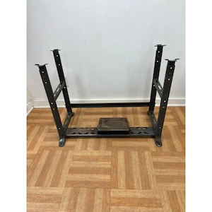 Può includere: Una base per tavolo in metallo grigio scuro con quattro gambe e un supporto centrale rettangolare. Le gambe sono angolate e presentano più fori per il fissaggio. La base ha un'estetica vintage e industriale.