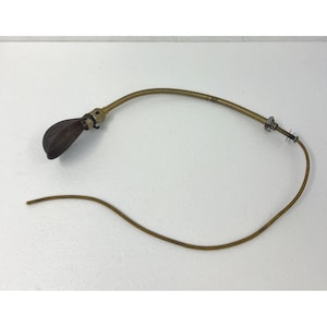 Può includere: Una lampada da scrivania in stile vintage con un collo di cigno flessibile color ottone e un paralume a forma di goccia marrone scuro. La lampada ha una base color ottone e un filo marrone. La lampada è regolabile.