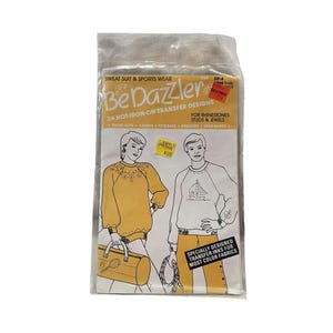 May include: A package of 24 iron-on transfer designs for sweatsuits and sports wear. The package includes designs for rhinestones, studs, and jewels. The designs are for use on sweatsuits, t-shirts, tote bags, sweaters, and headbands. The package is labeled "Be Dazzler" and includes a price tag of $3.29.