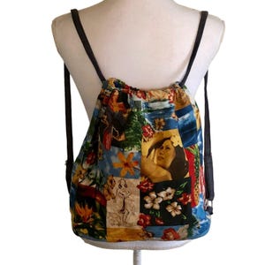 May include: A drawstring backpack featuring a vibrant collage print of tropical scenes, including hula dancers, hibiscus flowers, pineapples, and ocean waves. The bag has dark brown cord straps and a gathered top closure, displayed on a mannequin.