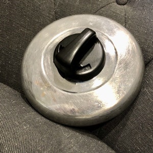 May include: A silver metal lid with a black plastic handle. The lid has a smooth, shiny surface.