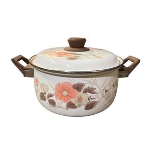 May include: White enamel cooking pot with a lid, featuring a floral design in shades of peach, brown, and cream. The pot has wooden handles and a wooden knob on the lid. The pot is a vintage kitchenware item.