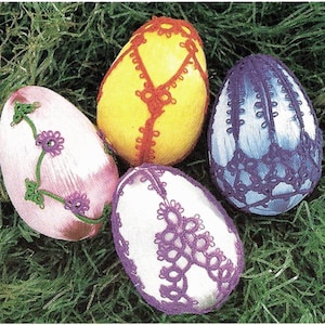 May include: Four decorated Easter eggs in shades of pink, yellow, white, and blue. The eggs are adorned with intricate lace and floral designs. The eggs are displayed on a bed of green grass.