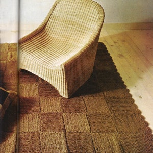 Puede incluir: Una silla de mimbre tejida de color marrón claro se encuentra sobre una alfombra de crochet marrón con borde festoneado.