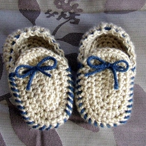 May include: A pair of crocheted baby booties in beige with blue trim and blue ribbon bows.
