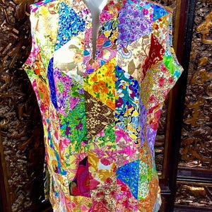 May include: A sleeveless, multi-coloured patchwork vest with a mandarin collar and a V-neckline. The vest is made of various floral patterned fabrics in shades of pink, blue, green, yellow, and red.