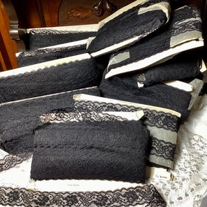 May include: A stack of black lace trim, packaged on white cardboard with the text "36 YDS" visible. The lace is delicate and has a floral pattern.