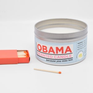 The Obama Scented Candle arranged next to a matchbox, so you can see that it is significantly larger than a matchbox.