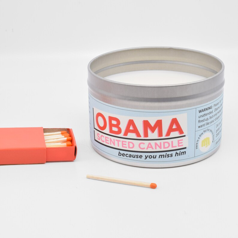 The Obama Scented Candle arranged next to a matchbox, so you can see that it is significantly larger than a matchbox.