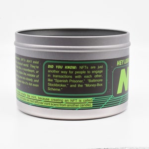 May include: A silver tin candle with a black and green label. The label has the text "HEY LOOK" and "N" in a large font. The text "DID YOU KNOW: NFTs are just another way for people to engage in transactions with each other, like "Spanish Prisoner," "Baltimore Stockbroker," and the "Money-Box Scheme." is also on the label.