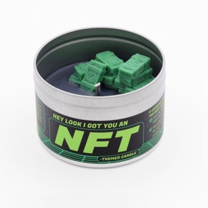 May include: A silver tin candle with a green and black label that says "Hey look I got you an NFT -themed candle". The candle is topped with green wax shaped like stacks of money.