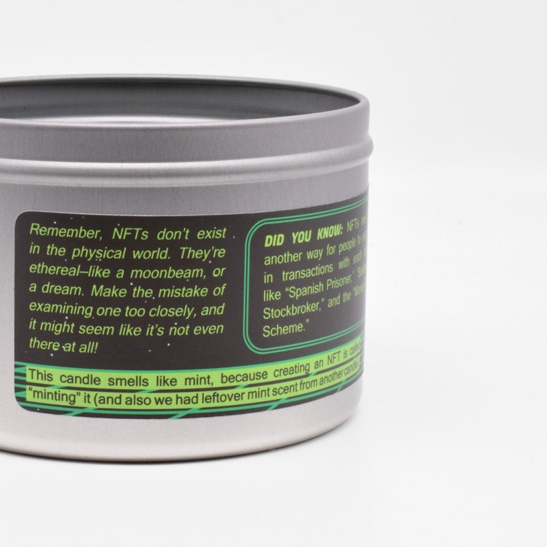 May include: A silver tin candle with a green and black label. The label reads "Remember, NFTs don't exist in the physical world. They're ethereal-like a moonbeam, or a dream. Make the mistake of examining one too closely, and it might seem like it's not even there at all!" and "DID YOU KNOW: NFTs are another way for people to engage in transactions with each other, like "Spanish Prisoner", "The Stockbroker", and the "419 Scheme.""