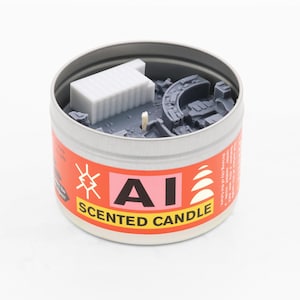 May include: A round metal tin containing a grey wax candle with a white rectangular structure and curved architectural elements embedded inside. The orange label features the text AI SCENTED CANDLE in black and white with graphic symbols.