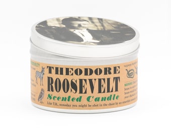 Könnte beinhalten: Eine runde silberne Metalldose mit Kerze und einem Deckel, der ein schwarz-weißes Porträt von Theodore Roosevelt zeigt. Das beigefarbene Etikett trägt den Text THEODORE ROOSEVELT SCENTED CANDLE in Schwarz und Grün sowie kleine Illustrationen eines Zebras und einer Eule.
