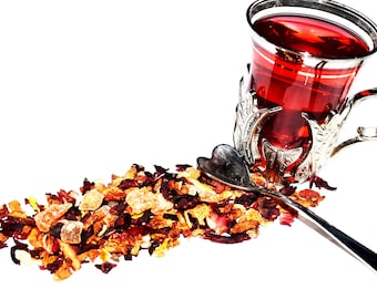 May include: A glass cup with a silver holder filled with red tea, a silver heart-shaped spoon, and a pile of dried fruit and flower tea leaves.